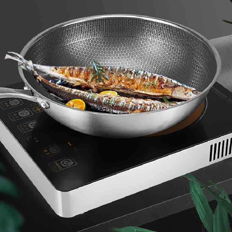 Wok med to stegte fisk og citrusskiver på en sort bordkogeplade