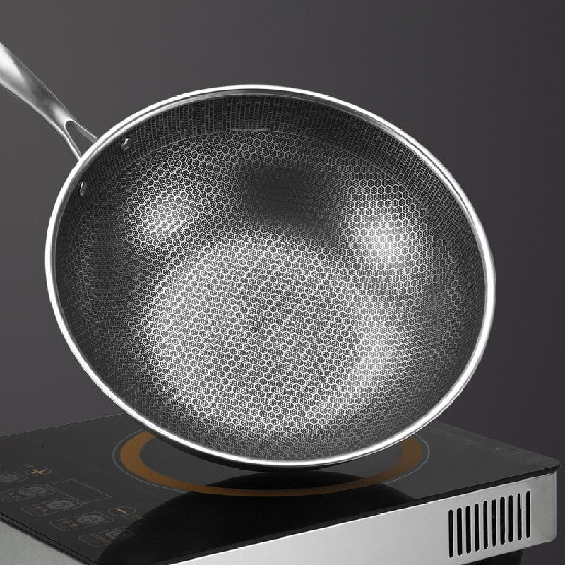Wok i rustfrit stål set ovenfra på en sort kogeplade mod en mørk baggrund