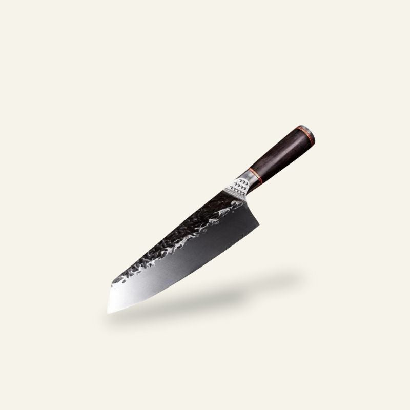 Le Naifu japansk kniv med højt blad, mørk hamret overflade og mørkt træskaft, fotograferet på lys baggrund