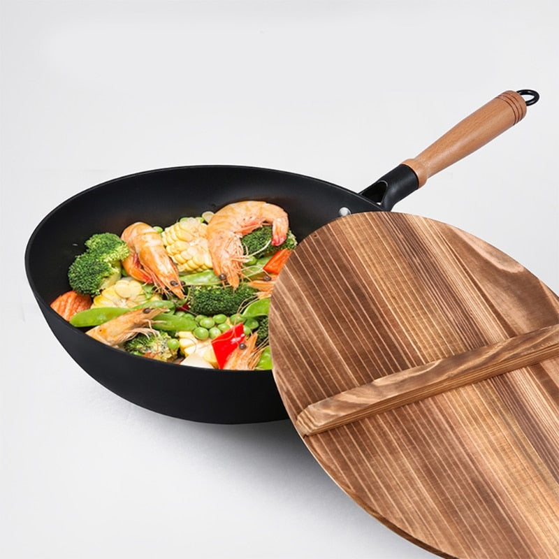Sort wok med træskaft fyldt med rejer og grøntsager, med trælåget stillet op foran