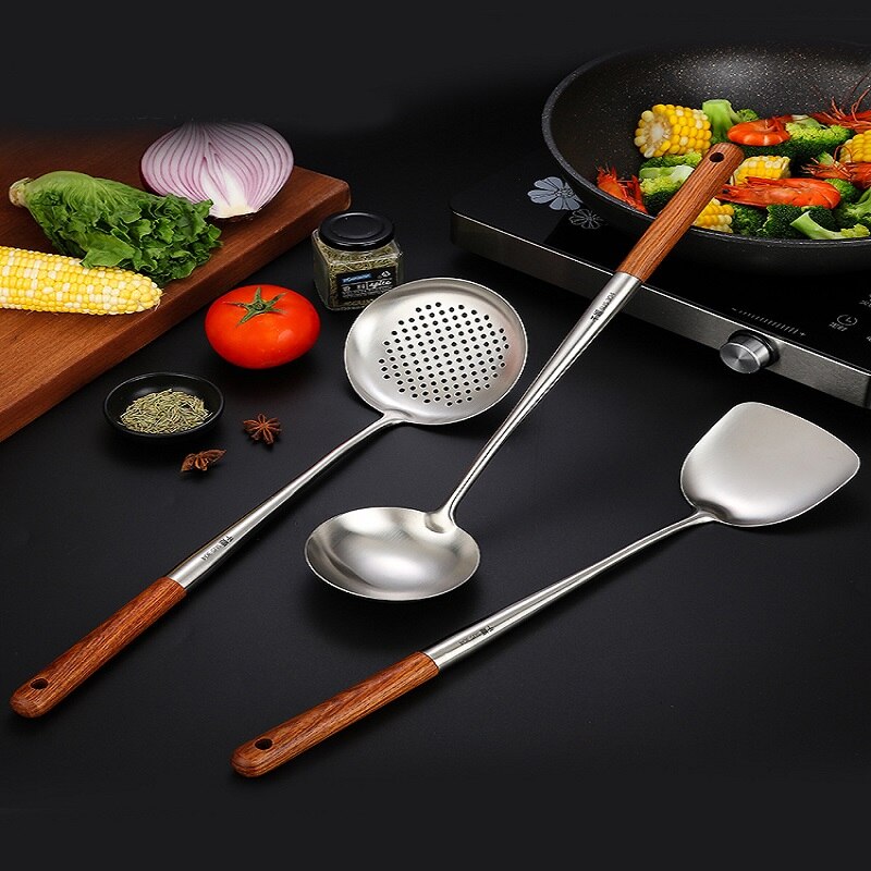 Woksigte, øseske og wokpalet på et mørkt bord foran en wok med majs, broccoli og rejer på en kogeplade