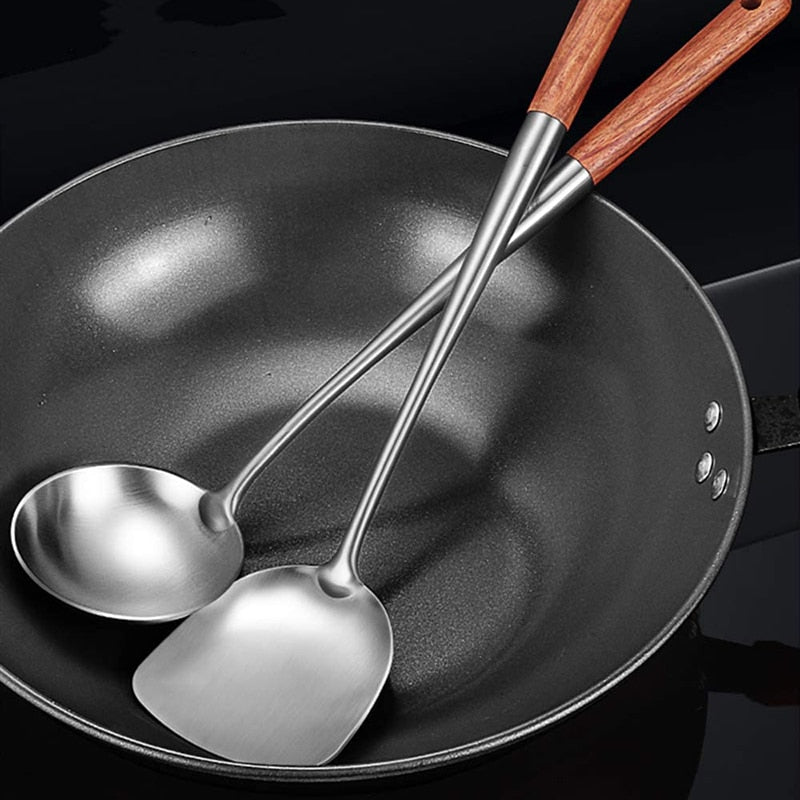 Wokpalet og øseske i stål med træskaft lagt ned i en sort wok