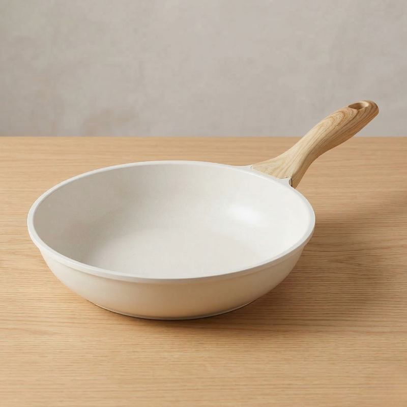 Cremehvid keramisk pande med lyst håndtag, stillet på et bord af lyst træ