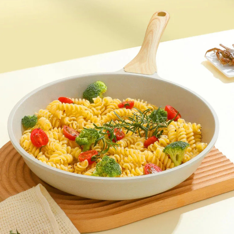 Pasta med broccoli og tomater i den lyse pande, set skråt ovenfra på et træbræt