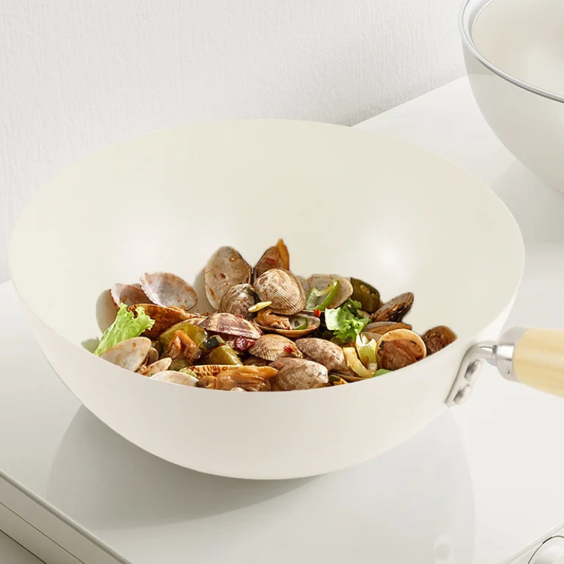 Muslinger med grønt og peberfrugt i den cremefarvede wok på et hvidt køkkenbord