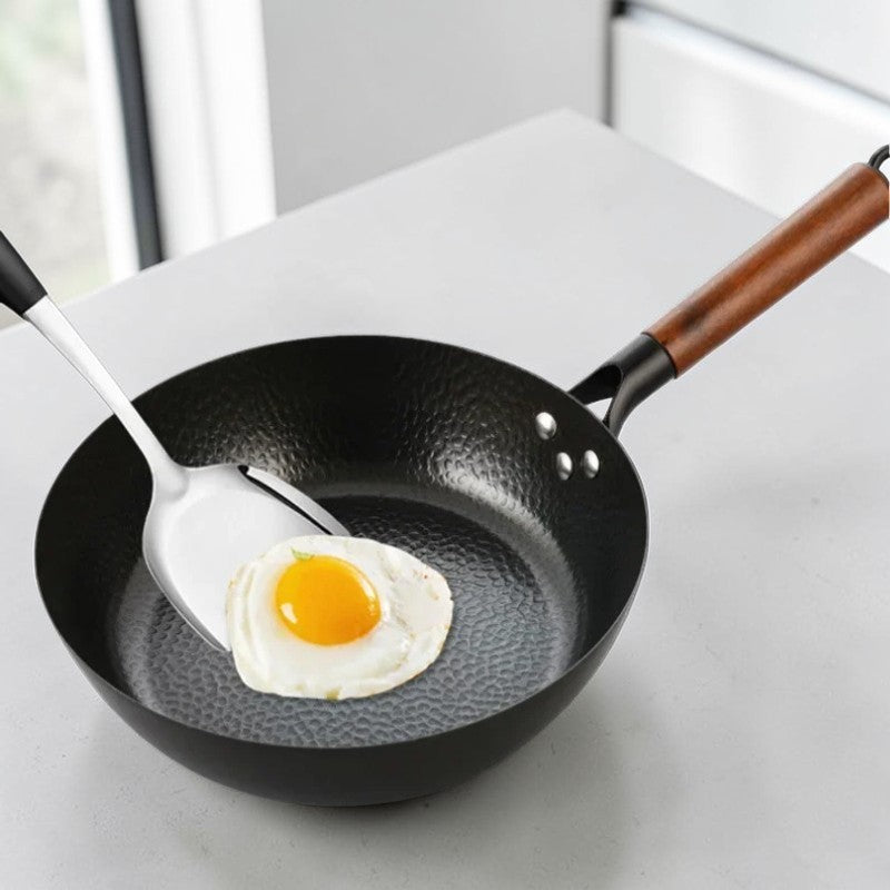 Spejlæg i den hamrede wokpande med en stålspatel, på et lyst køkkenbord