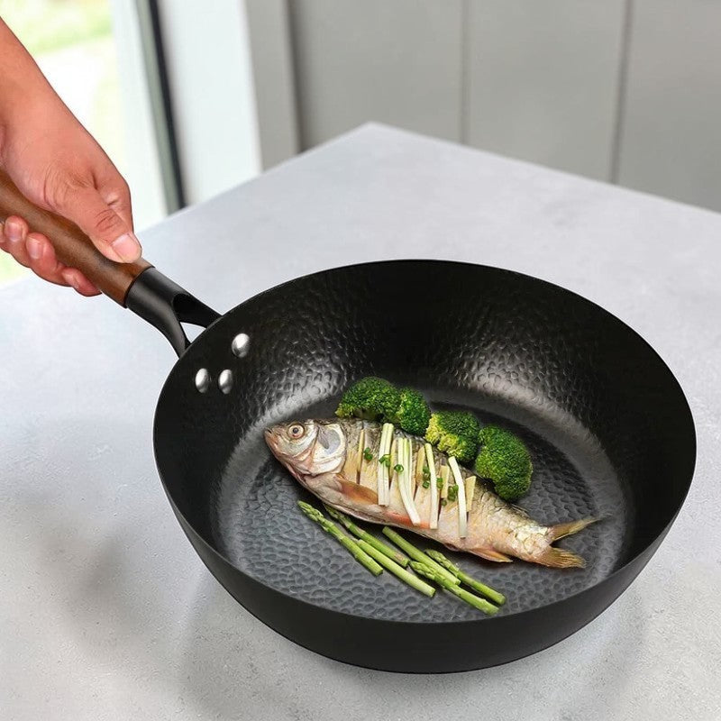 Hånd holder træhåndtaget på wokpanden med en hel fisk, broccoli og grønne asparges