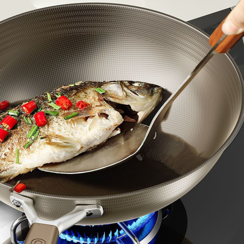 Nærbillede af en hel stegt fisk med chili og forårsløg, som løftes med en spatel i wokken over gasblusset
