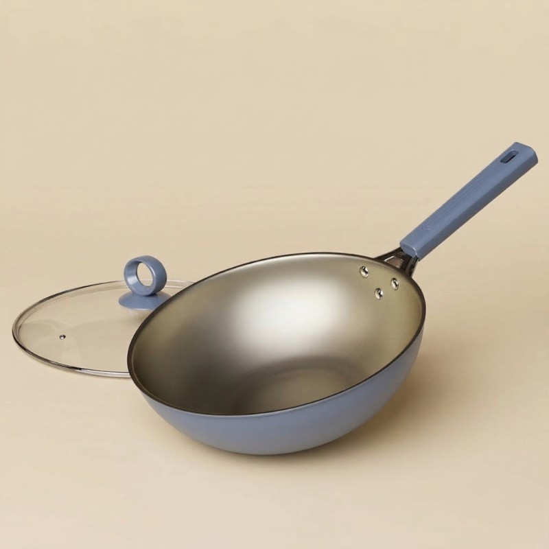 Le Maroki wok gryde i blågrå med guldfarvet inderside og langt skaft, glaslåg med ringknop ved siden af på beige baggrund