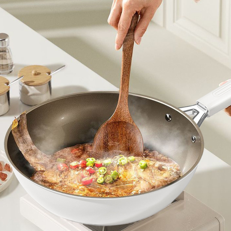 Hånd rører med træspatel i hvid wokpande med fisk i sauce og skiver af grøn og rød chili