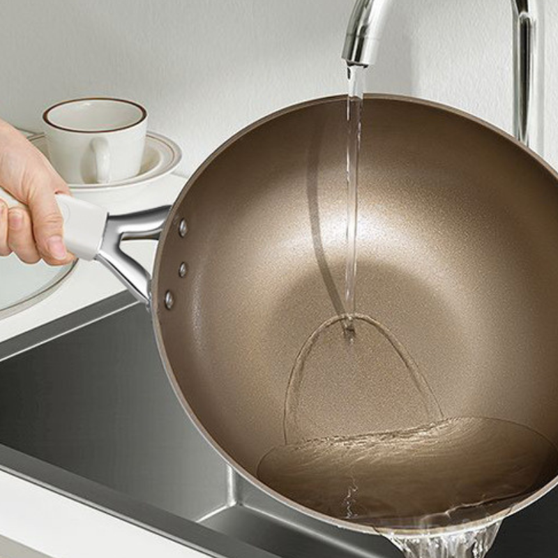 Indersiden af wokpanden skylles under vandhanen, mens en hånd holder i håndtaget