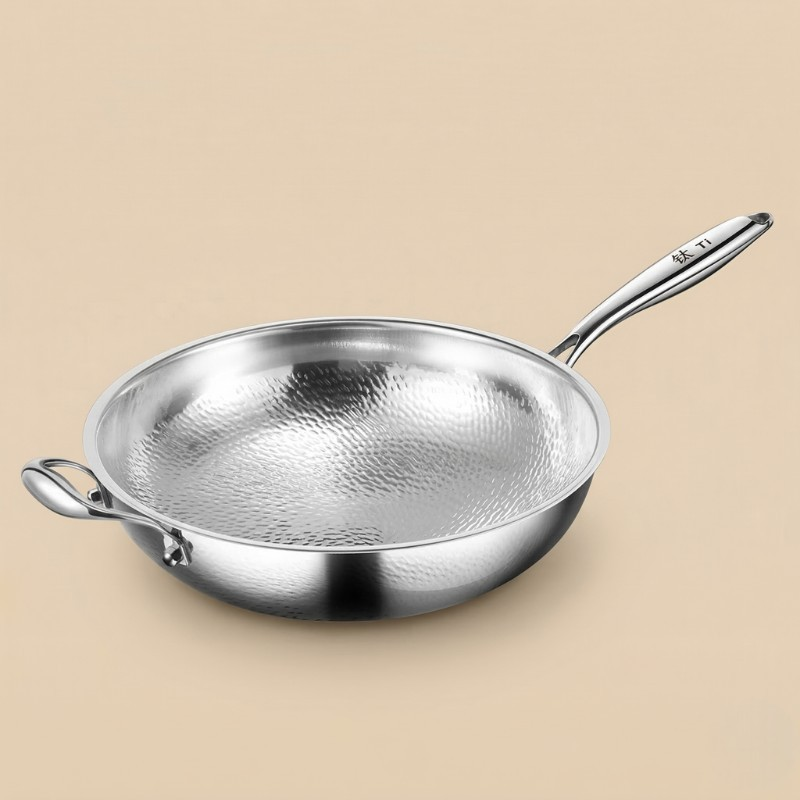 Wok i rustfrit stål uden låg set skråt ovenfra, så det hamrede mønster på indersiden ses, på beige baggrund