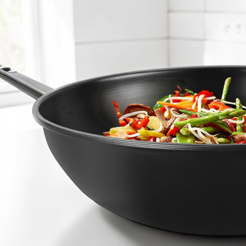 Sort wok med grøntsager, asparges og bønnespirer, set tæt på i et lyst køkken
