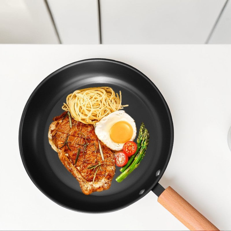 Stegepanden set ovenfra med en bøf, spaghetti, spejlæg, cherrytomater og asparges
