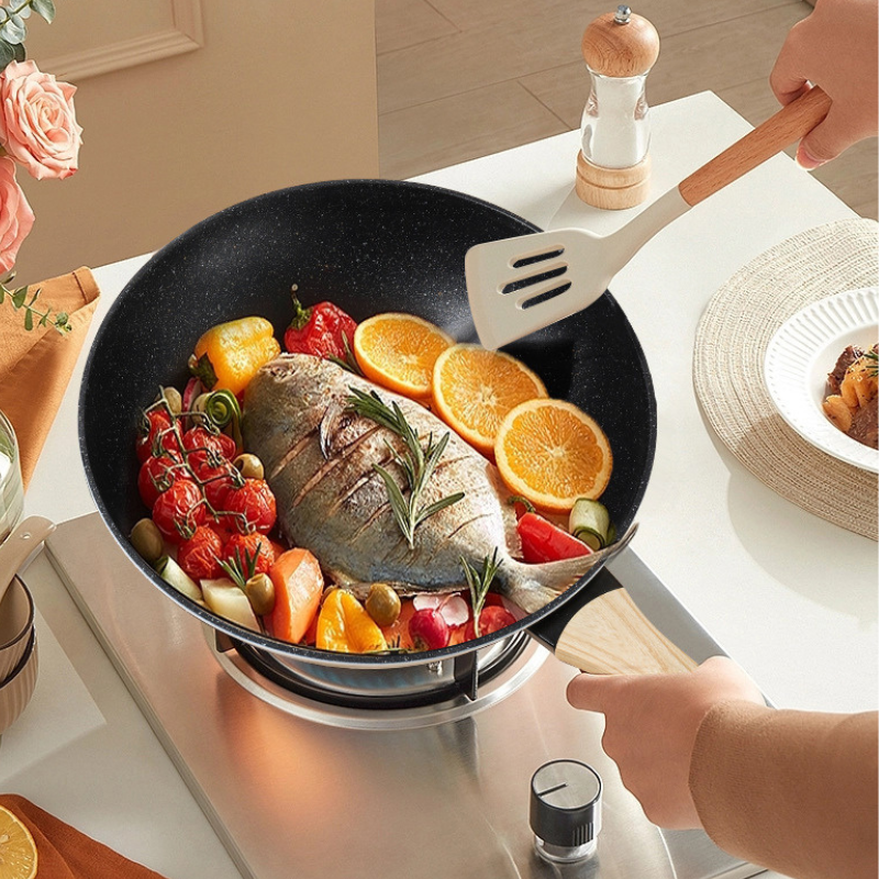 Hel fisk med appelsinskiver, tomater og grøntsager i wokpanden på et gasblus, en hånd vender med en hvid spatel