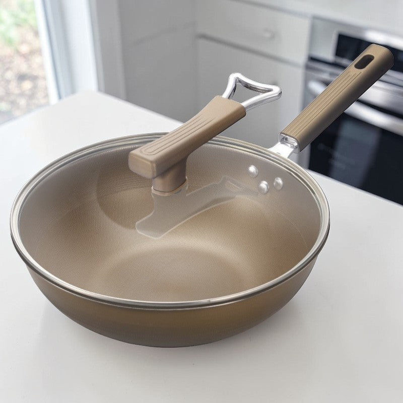 Wokpande med glaslåg på et hvidt køkkenbord med en ovn i baggrunden