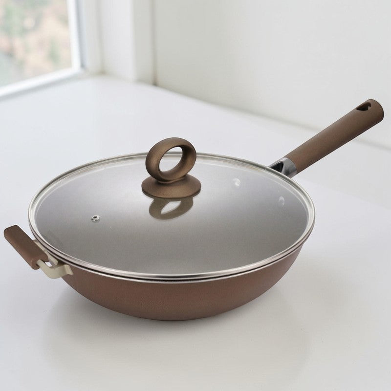 Wokpande med sidegreb og glaslåg med rund knop på en hvid bordplade ved et vindue