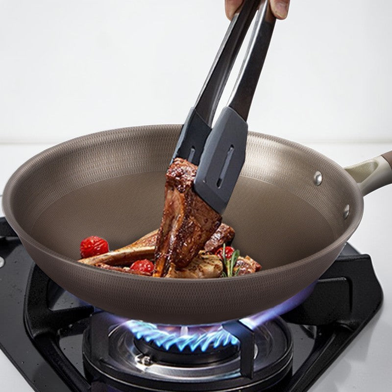 Lammekoteletter og tomater vendes med en tang i wokpanden over en blå gasflamme