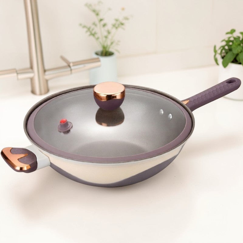 Wokken med glaslåg på et lyst køkkenbord foran en vandhane og krydderurter i potter