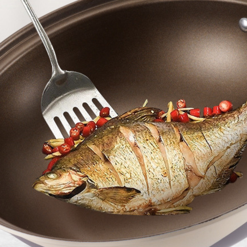 Helstegt fisk med hakket chili i wokken, vendt med en metalspatel