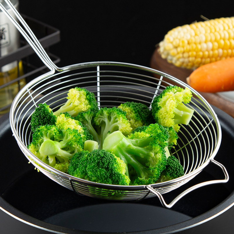 Fritureske fyldt med broccolibuketter holdt over en sort gryde, majskolbe og gulerod i baggrunden
