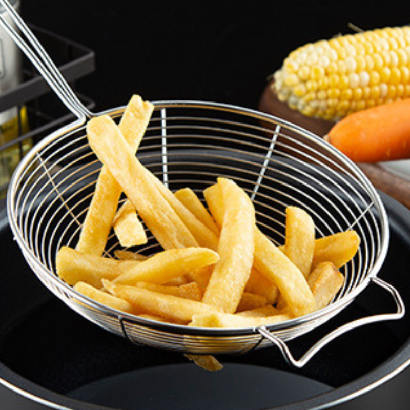 Pommes frites i fritureskeens trådkurv over en sort gryde med majs og gulerod bagved