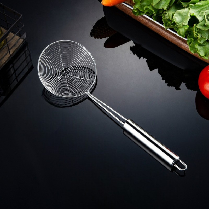 Fritureske med spiralformet trådkurv på en blank sort flade med salat og tomat i baggrunden