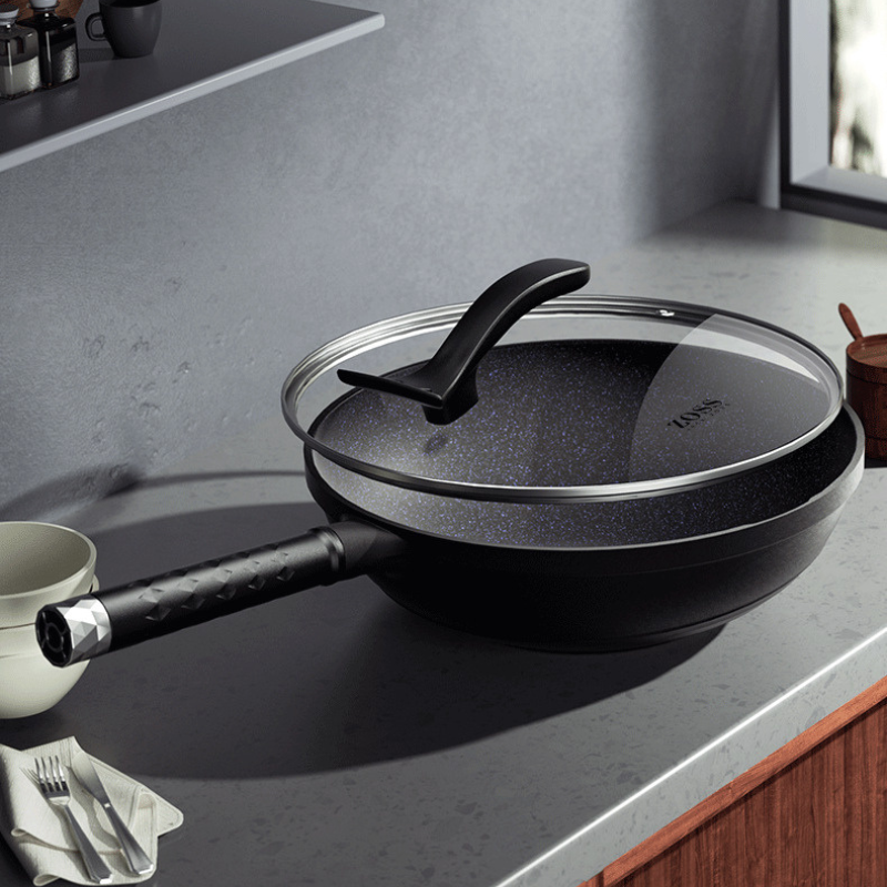Wok med glaslåg på et gråt køkkenbord, hvor den prikkede stenbelægning ses gennem glasset