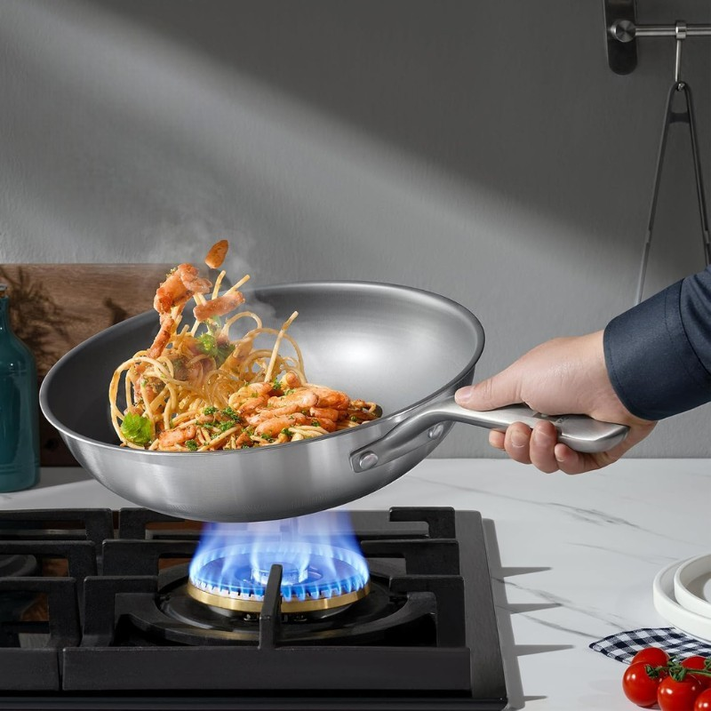 En hånd kaster rejer og spaghetti op i luften fra woken over et blåt gasblus