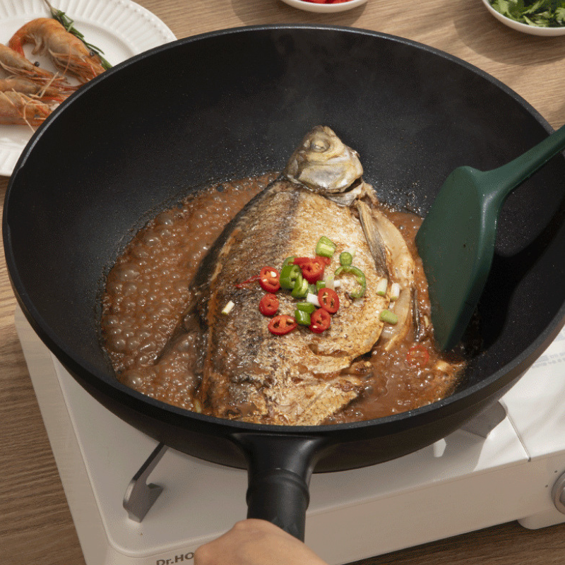 En hel fisk i brun sauce med chili og forårsløg i woken, med en grøn spatel og en tallerken rejer bagved