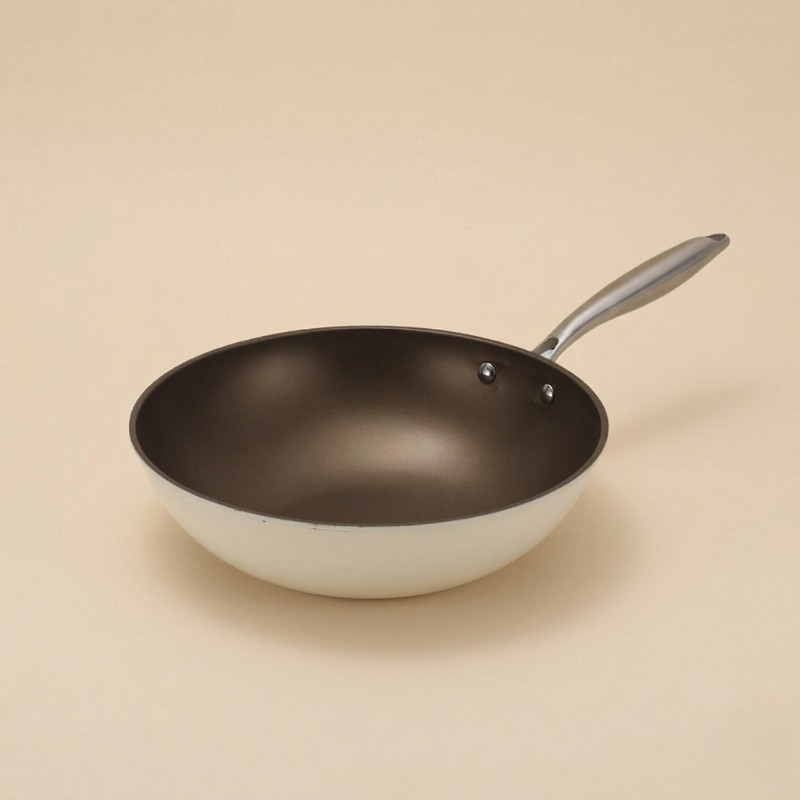 Hvid wokpande uden låg med mørk slip-let belægning indeni, på beige baggrund
