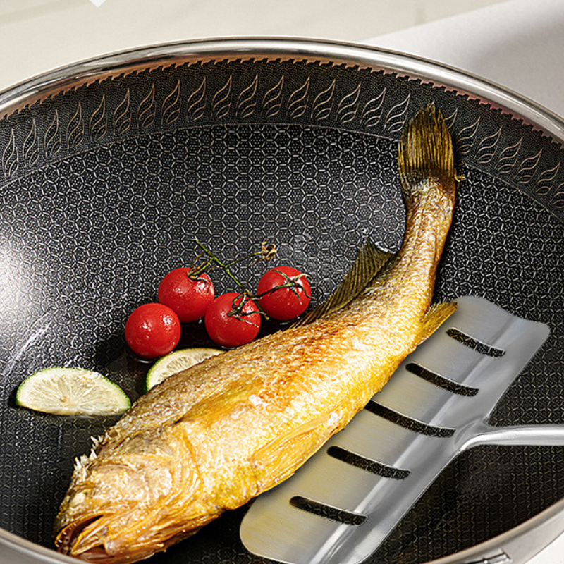 Bladet skubbet ind under en hel stegt fisk i en wok med cherrytomater og limeskiver