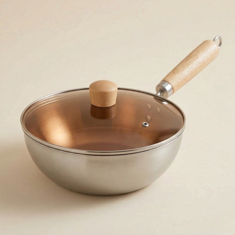 Le Nuriko stål wok i rustfrit stål med glaslåg og træhåndtag på en beige baggrund