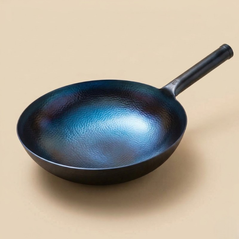 Le Kasoma blue carbon steel wok i blåt, hamret kulstål med sort skaft, fotograferet på en beige baggrund