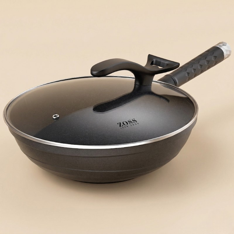 Le Komaga wok i sort med glaslåg og mønstret håndtag på en beige baggrund