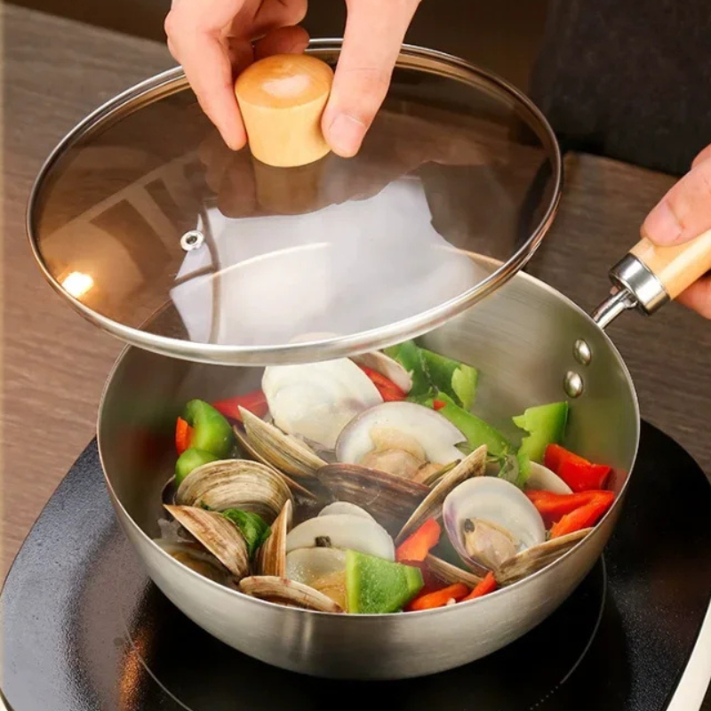En hånd løfter glaslåget af wokken med muslinger og peberfrugt
