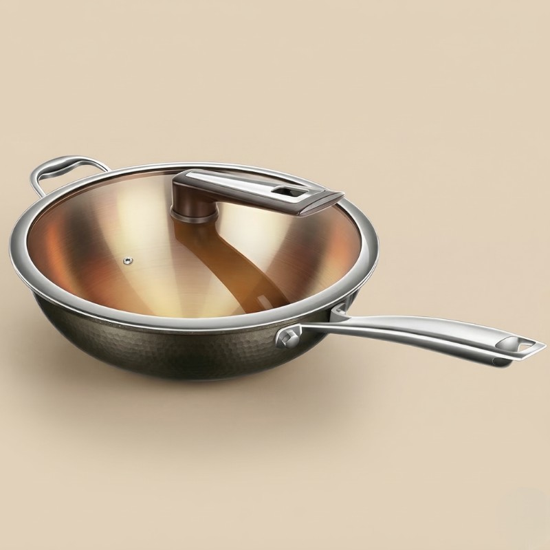 Le Houou wokpande i rustfrit stål med tonet glaslåg, langt skaft og sidehank, set skråt fra siden på beige baggrund