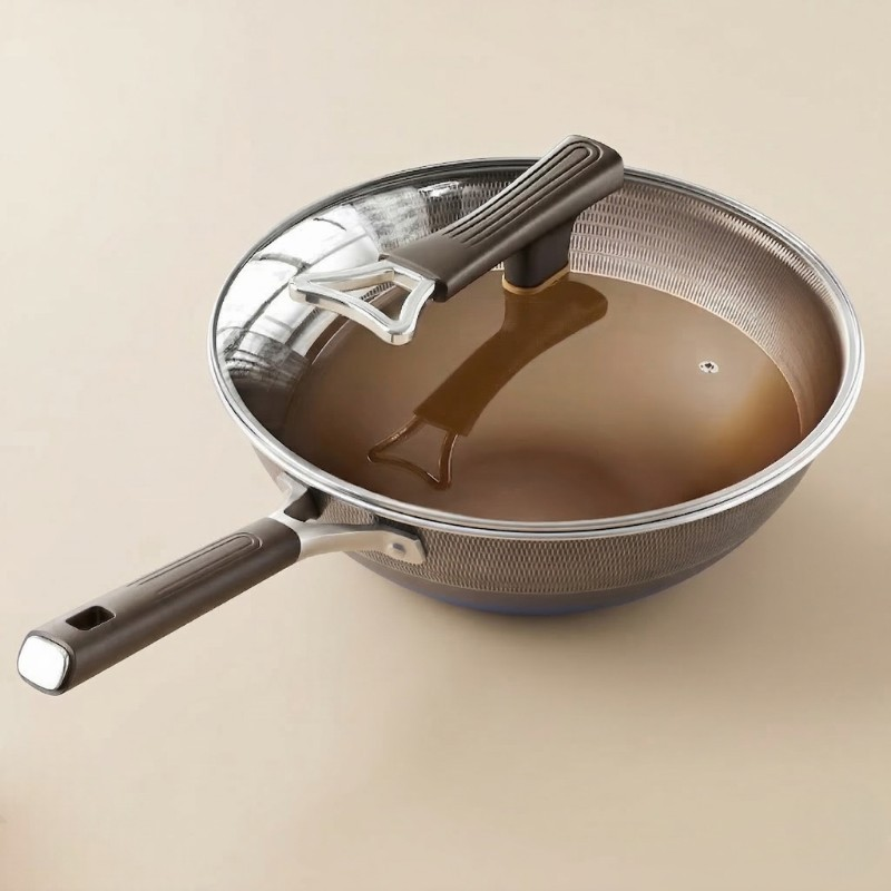 Le Chokai wok non-stick i rustfrit stål med glaslåget på, fotograferet mod en lys beige baggrund