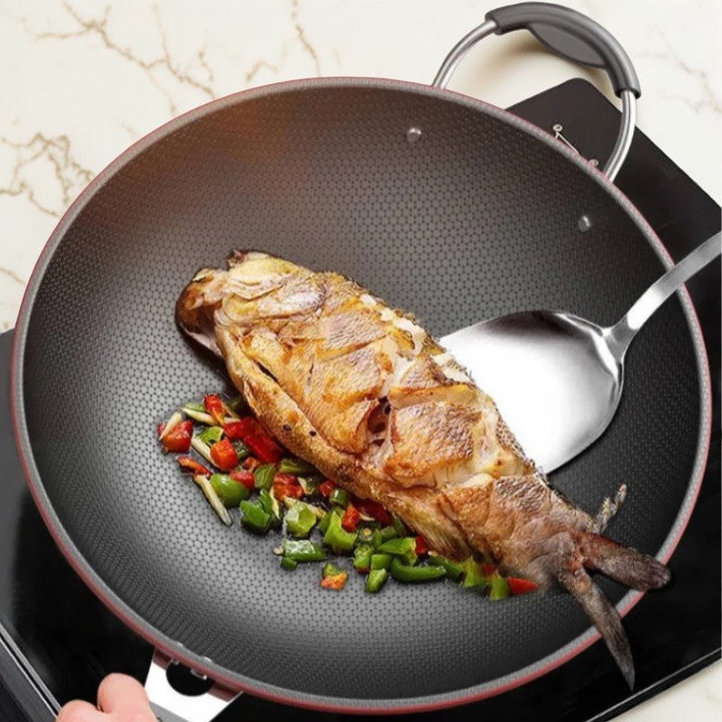 Hel stegt fisk med hakket peberfrugt i woken, vendt med en spatel på en sort kogeplade