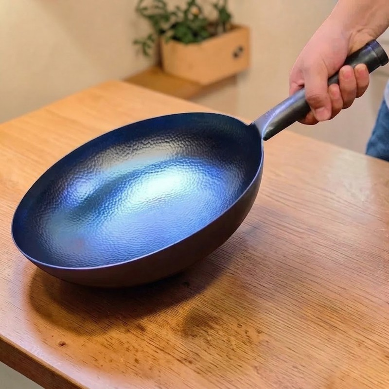 En hånd holder den blå wok i det sorte skaft over et træbord