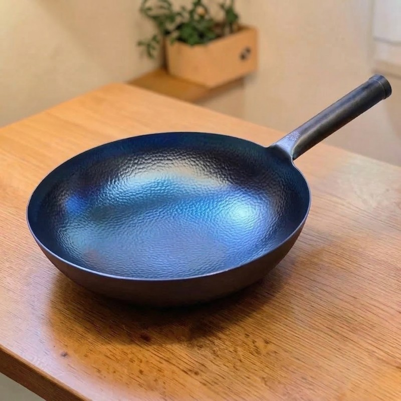 Blå wok med hamret overflade på et træbord, med en potteplante i baggrunden