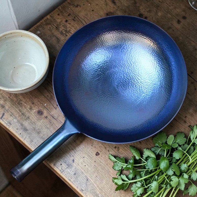 Den blå wok set ovenfra på et slidt træbord med en tom keramikskål og krydderurter