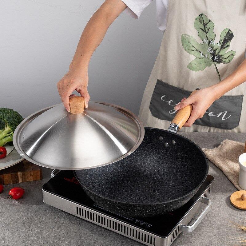En hånd løfter metallåget af wokken på en bordkogeplade, mens den anden hånd holder håndtaget