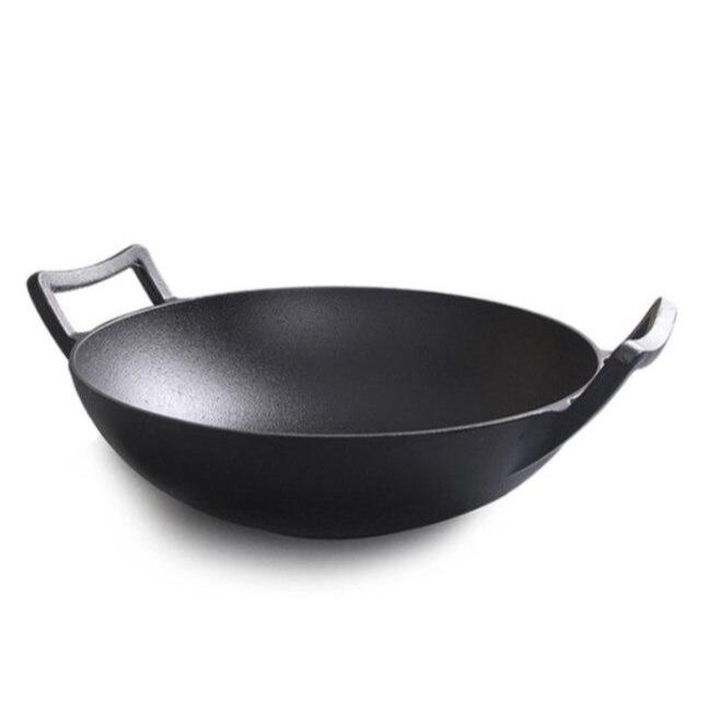 Sort wok i støbejern med en kort hank i hver side, set fra siden på hvid baggrund