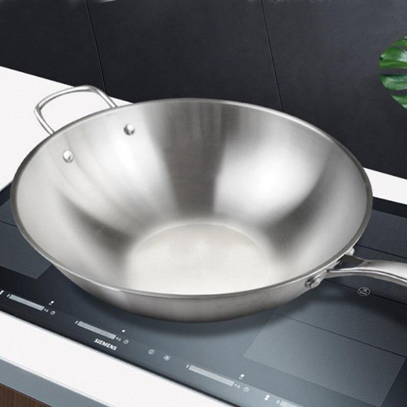Rustfri wokpande med hank på en sort induktionskogeplade i et køkken