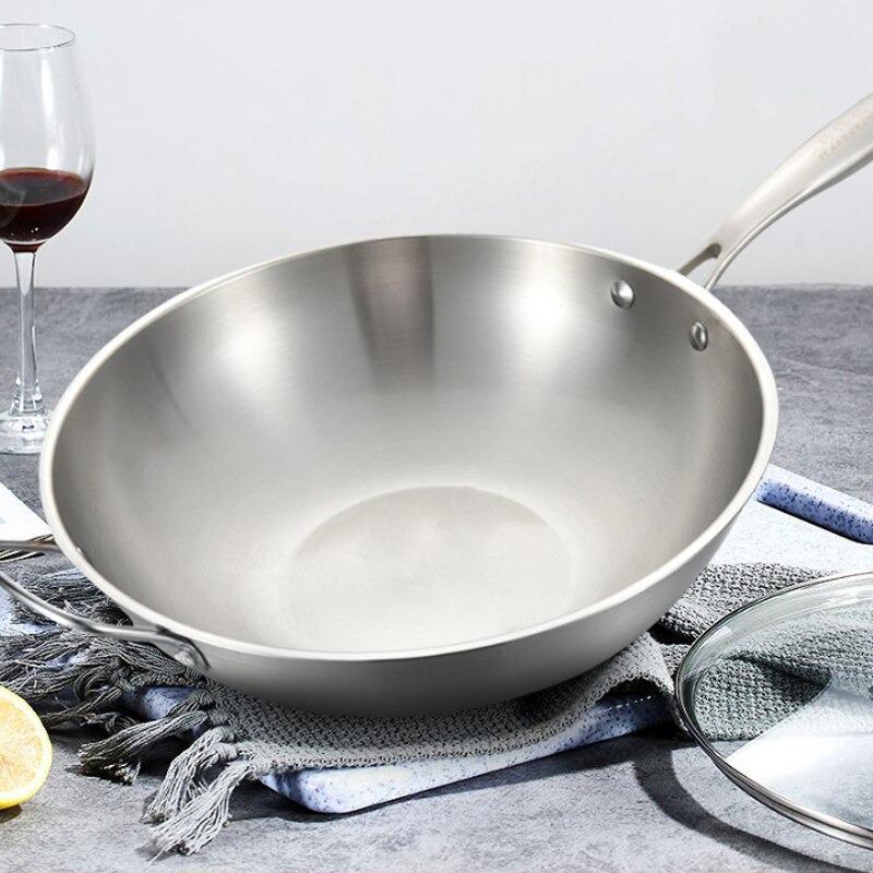 Rustfri wokpande med hank på et gråt viskestykke ved siden af et glas rødvin og en halv citron