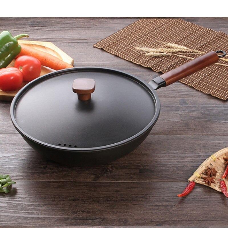 Jern wok med låg på et mørkt træbord med grøntsager og tørret chili omkring