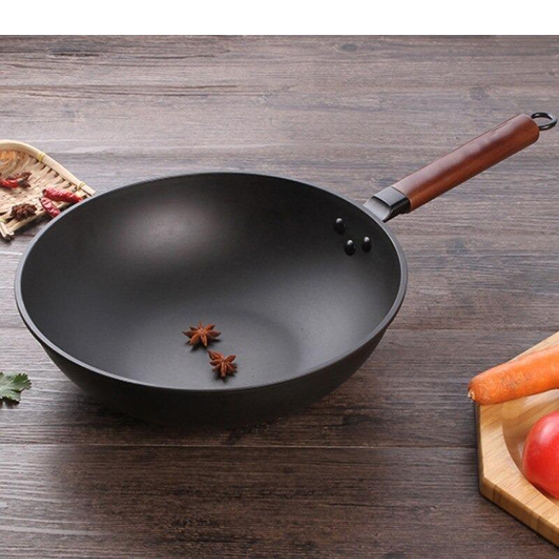 Åben jern wok uden låg med to stjerneanis i bunden, på et træbord med chili og grøntsager