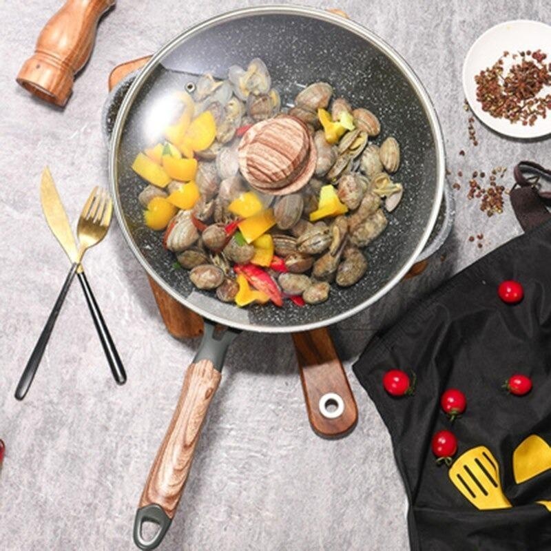 Wokken med glaslåg fyldt med muslinger og gul og rød peberfrugt, set ovenfra på et gråt bord