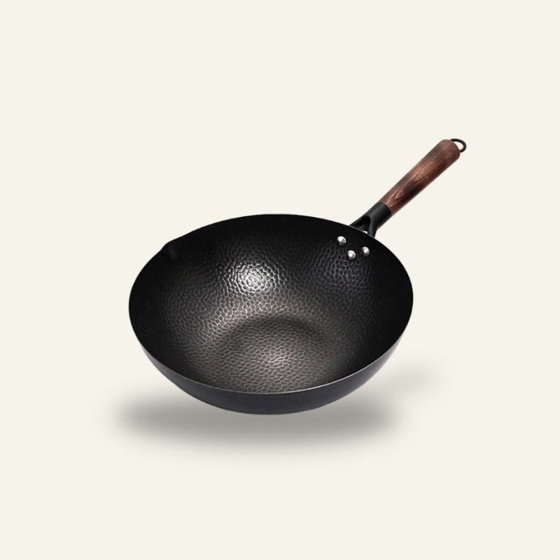 Le Bandai wok i jern med træhåndtag og små fordybninger indvendig, vist uden låg på lys baggrund